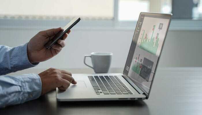 Establish a strong online presence | tycoonstory media Professional working on laptop and phone, analyzing data to build a strong brand through digital marketing strategies and business analytics.