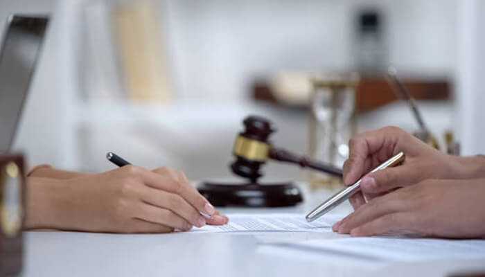 Filing the claim | tycoonstory media Hands of two individuals signing legal paperwork with a gavel and pen, representing the influence of social media algorithms in decision-making processes.