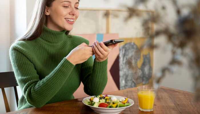 Fuel your body with clean nutrition | tycoonstory media A woman enjoying a healthy salad while using her phone, take charge of her health by staying connected and informed.