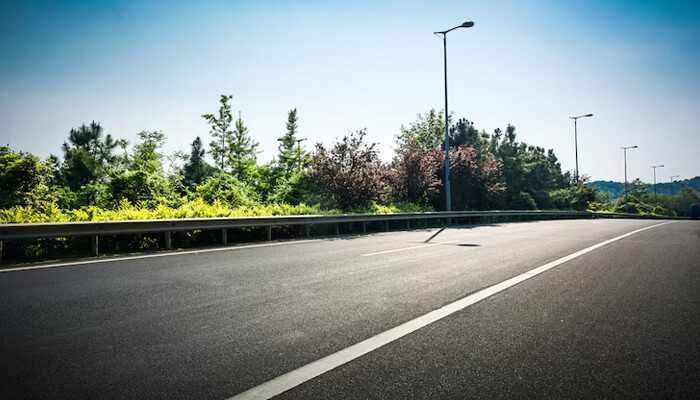 Growing trends in asphalt technology | tycoonstory media Clear asphalt road with greenery along the sides, highlighted by street lights, offering a scenic, open roadway view.