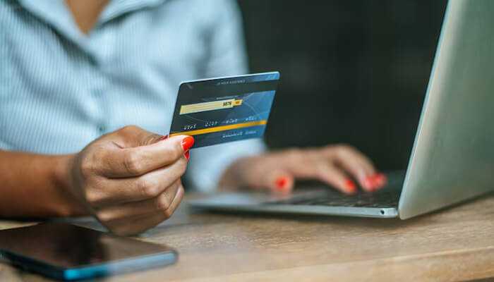 Hdfc bank millennia credit card benefits | tycoonstory media A person holding the hdfc bank millennia credit card while using a laptop for online shopping.