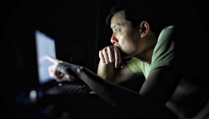 How screen time impacts adults | tycoonstory media Individual focused on a computer screen in a dark room, representing late-night screen time and digital engagement.