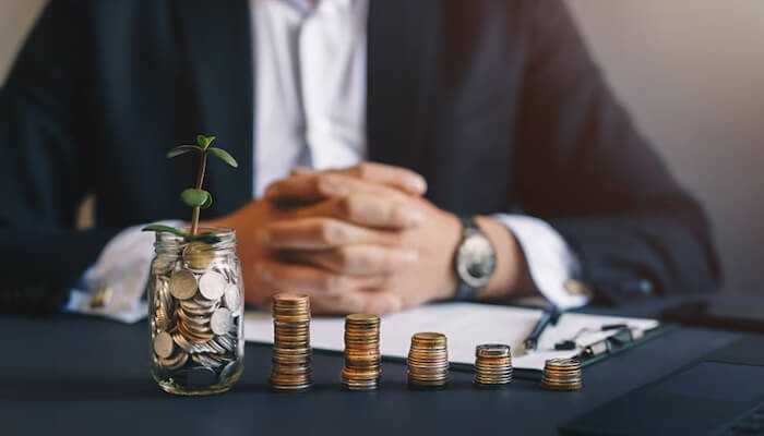 How you can make the most of your elss investment | tycoonstory media Businessman sitting behind growing stacks of coins and a jar with a plant, representing wealth creation through elss mutual fund planning.