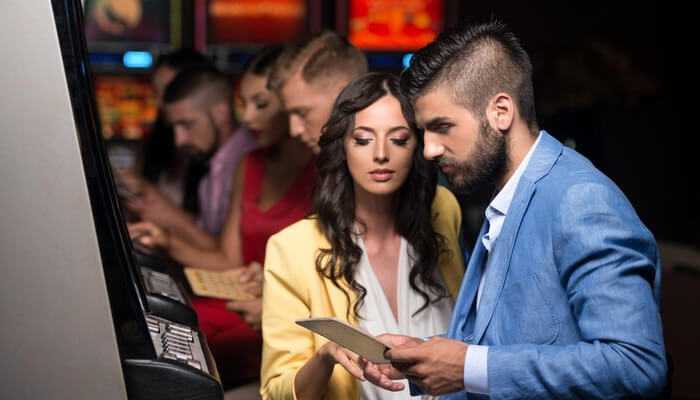 Its not just flashing lights and luck | tycoonstory media A couple of people playing online slots at a casino, looking at the screen and interacting with the game interface.