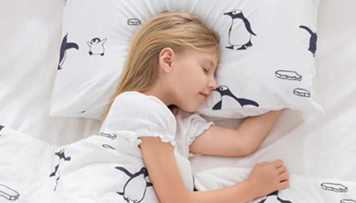 Kids sleeping blankets | tycoonstory media A child resting comfortably with penguin-printed bedding, illustrating how soft, cozy environments support childrens sleep needs effectively.