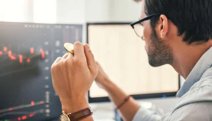 Private liquidity is quietly winning | tycoonstory media Individual analyzing cryptocurrency market data on dual monitors, holding a coin, reflecting the strategic decisions in the liquidity wars of crypto trading.