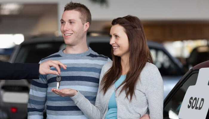 Reduced insurance and registration fees 1 | tycoonstory media A happy couple receiving car keys after buying a second hand vehicle, with a'SOLD' sign visible in the background.