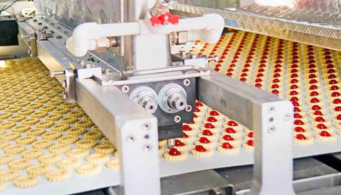 Switching products without cross-contamination | tycoonstory media A close-up of automated machinery in action, producing food items with precision. This highlights the importance of technology and food and beverage ingredients in modern production lines.