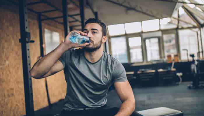 Tips for maintaining energy levels on a low-carb diet | tycoonstory media Man drinking water during a workout in the gym, taking a break while following a low-carb diet.