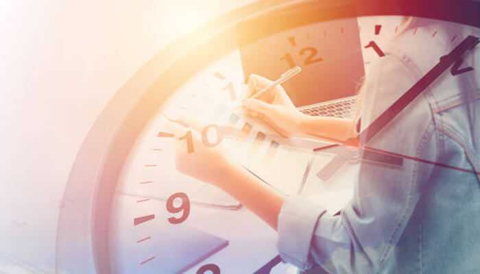 Turn usual leisure into practical activities | tycoonstory media A close-up of a person writing in a notebook with a large clock superimposed, symbolizing time management and productivity, to overcome procrastinate.