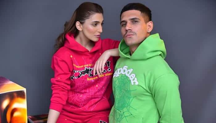 Why the spider hoodie is more than a trend | tycoonstory media Man and woman posing in vibrant green and red spider hoodies with unique graphic designs, representing modern streetwear style.
