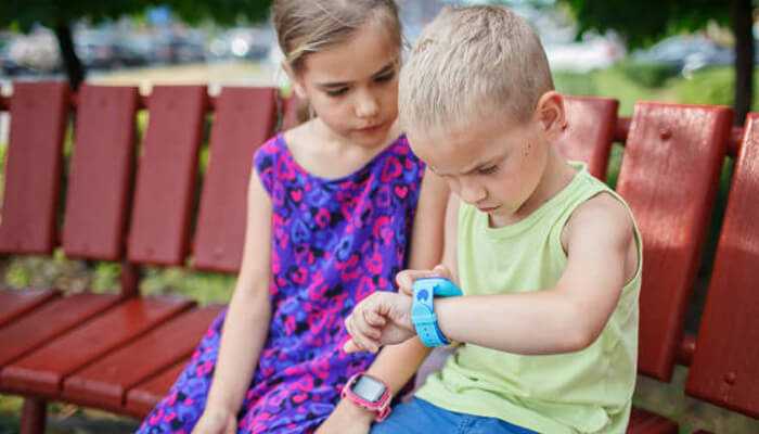 Compatibility with smartphones | tycoonstory media Two children sitting on a bench, both wearing gps watches for kids, as one boy interacts with his smartwatch while the girl watches curiously.