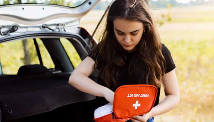 Dressings and bandages 1 | tycoonstory media Young woman accessing a vehicle first aid kit from her car trunk, ensuring road safety and emergency readiness.