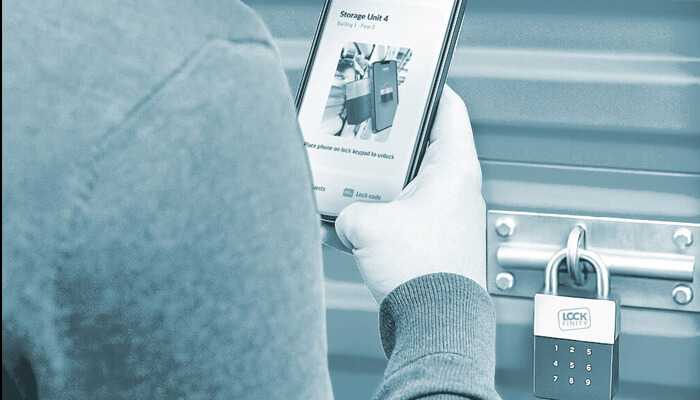 Enter lockfinity | tycoonstory media Person using a smartphone to unlock a smart padlock on a storage unit, demonstrating advanced security technology in storage facilities.