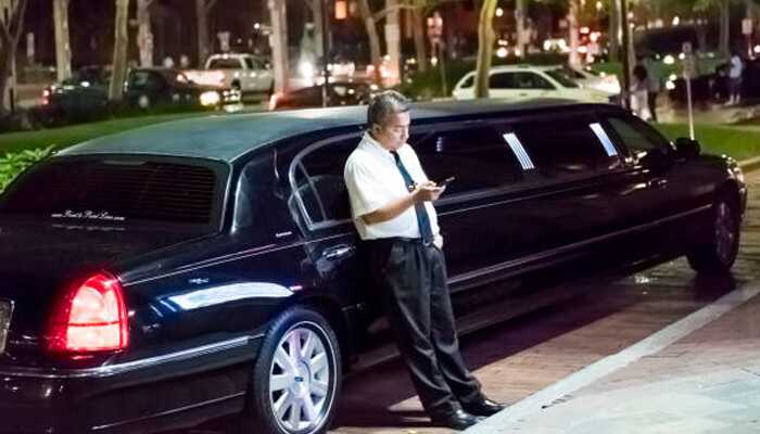 How limo companies benefit behind the scenes | tycoonstory media Chauffeur waiting beside black limousine during a night event — ideal representation for limousine booking experience.