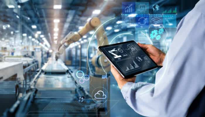 Manufacturing data integration 1 | tycoonstory media A professional monitoring factory operations using a tablet, displaying real-time factory insights through digital interfaces and data analytics.