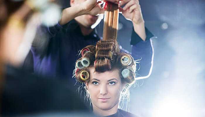 Multi-functional attachments 1 | tycoonstory media Woman sitting at a salon with heatless hair curlers in her hair while a stylist carefully works on the front section.
