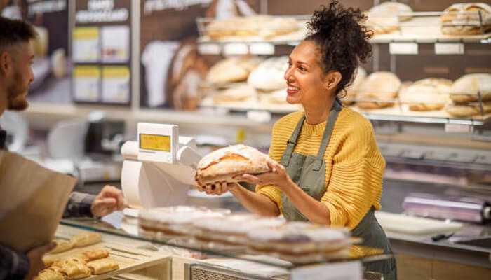 Offering locally tailored products or services | tycoonstory media Female bakery owner smiling while serving a customer, representing the spirit of local entrepreneurship in community-focused businesses.