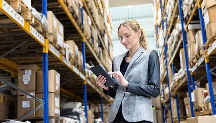 Order management efficiency | tycoonstory media Businesswoman managing inventory in warehouse using tablet, illustrating sourcing through online distributors and order management.