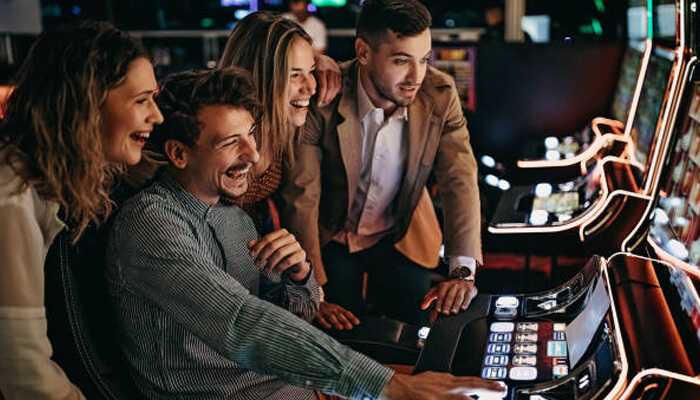 Popular casino games | tycoonstory media A group of friends enjoying one of the four fun games to play with friends at a lively casino, sharing laughs around a slot machine.