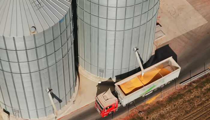 Reducing reliance on middlemen | tycoonstory media A red truck being loaded with grain from large metal silos at an agricultural facility, showcasing efficient grain management operations.