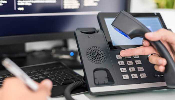 Restrict access and segment your network | tycoonstory media Voip security in business communication: close-up of a person dialing on a voip office phone next to a computer screen
