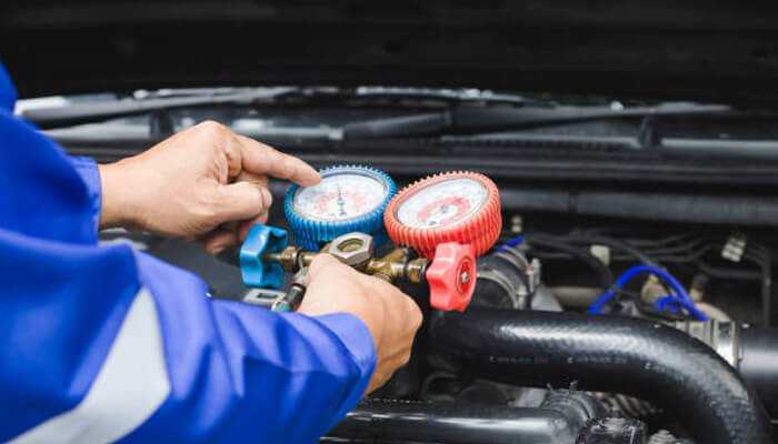 Signs your car ac needs immediate attention | tycoonstory media Mechanic performing car ac repair by checking refrigerant pressure levels under the vehicle hood.