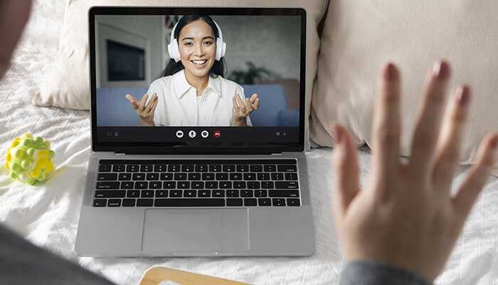 Video chat sites | tycoonstory media Individual engaging in a one-on-one video chat on a laptop, smiling and waving while using a random video chat site.