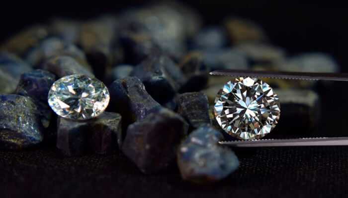 What makes some diamonds sparkle more | tycoonstory media Two polished diamonds, one held by tweezers and the other resting on uncut stones, showcasing brilliance and clarity—explore more about the diamond cut grades that determine their sparkle and value.