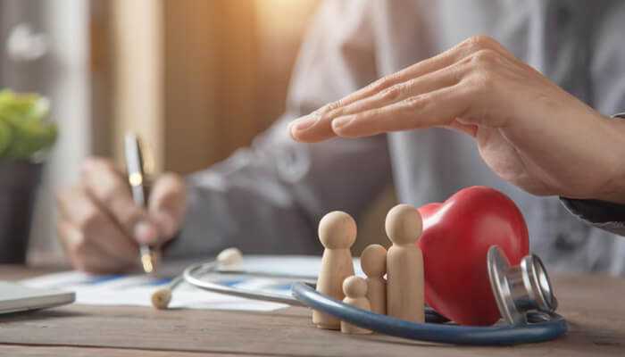 Why do small businesses require group health insurance | tycoonstory media Hand covering a wooden family figure next to a stethoscope and red heart, representing the security and benefits provided by group health insurance for employees.