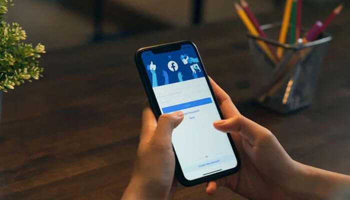 Why should you use facebooks restricted list - tycoonstory | tycoonstory media Close-up of a hand holding a phone displaying the facebook login screen, demonstrating how to restrict someone on facebook.