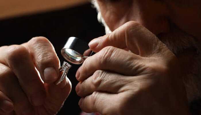 Why their credentials actually matter when youre buying | tycoonstory media Experienced gemologist examining a diamond ring using a jeweler’s loupe for clarity and authenticity assessment.