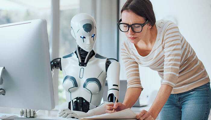 Creating a culture of collaboration and innovation - tycoonstory | tycoonstory media Human collaborating with a humanoid robot on a computer, representing gen-ai integration in startups and future workplace innovation.