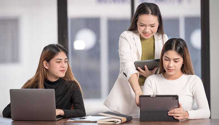 Entrepreneurship guides - tycoonstory | tycoonstory media Three women in a business meeting, collaborating on new learning experiences using digital devices.