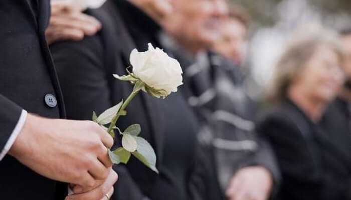 Unseen rituals Close-up of a person holding a white rose at a memorial service, symbolizing unseen rituals of grief, tribute, and silent farewell.