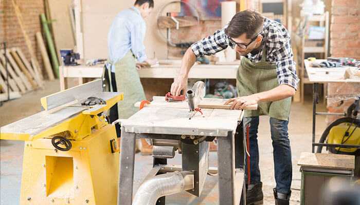Overlooking the joinery details - tycoonstory | tycoonstory media Skilled worker in a workshop during a commercial fit-out project, cutting wood to create custom furniture for an office space.