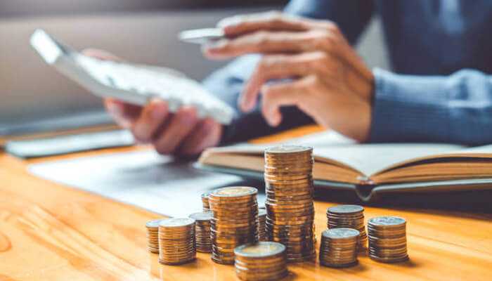 Pay yourself first 1 | tycoonstory media An individual using a calculator to manage finances and plan a budgeting method, with coins stacked on the table, illustrating personal financial planning and savings.