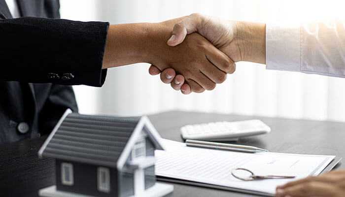 Reevaluate your insurance coverage - tycoonstory | tycoonstory media Business handshake representing agreement on mortgage terms, with house model and documents on the table.