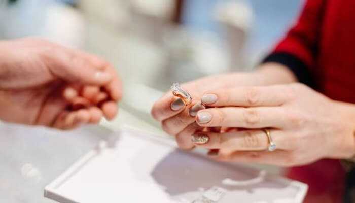 Spotting flaws that matter | tycoonstory media A jeweler’s hands carefully holding a sparkling diamond engagement ring to show a customer over a glass display case in a luxury jewelry store.