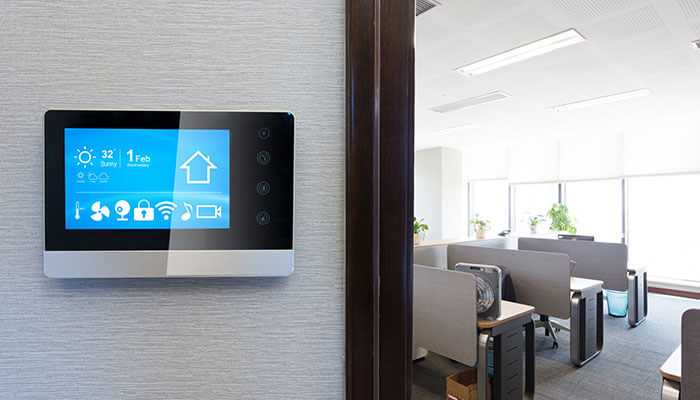 Use smart tech but dont overcomplicate it - tycoonstory | tycoonstory media Smart thermostat on the wall of a bright, energy-efficient office, highlighting the use of technology in office renovations.