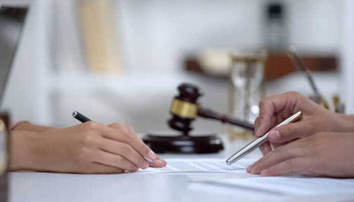 Personal injury settlement Lawyer and client reviewing and signing legal documents with a gavel in the background, representing a personal injury settlement agreement.