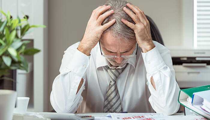 Bankruptcy and personal insolvency - tycoonstory | tycoonstory media Senior businessman with head in hands at desk, illustrating the consequences of misconduct and director disqualification in uk.