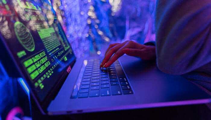 Constantly changing cyber threats - tycoonstory | tycoonstory media Hacker coding on a laptop in dark lighting, symbolizing shopify malware attacks and cyber threats targeting e-commerce stores.