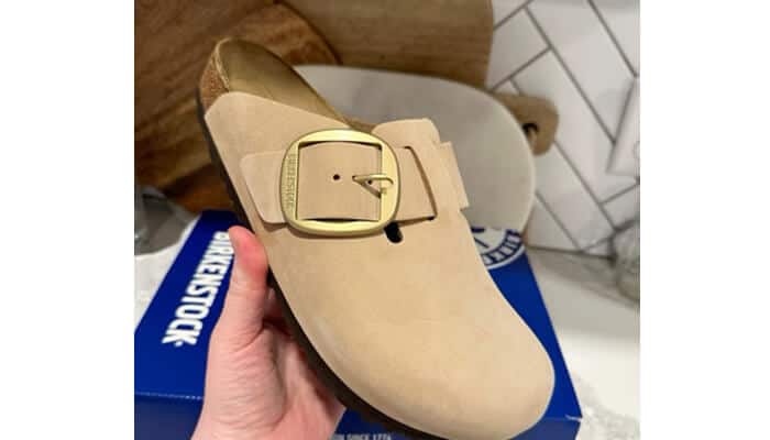 How i brought my cork-latex footbed back to life 1 | tycoonstory media Hand holding a beige birkenstock clog with a gold buckle over a branded shoe box — footwear cleaning hack for keeping suede clogs clean.