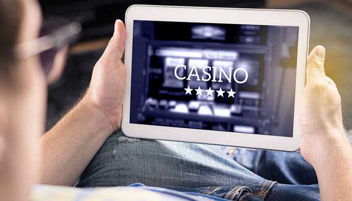 Learn the basics before betting real money | tycoonstory media Person holding a tablet displaying a casino app screen, symbolizing digital gaming trends in online casino malaysia.