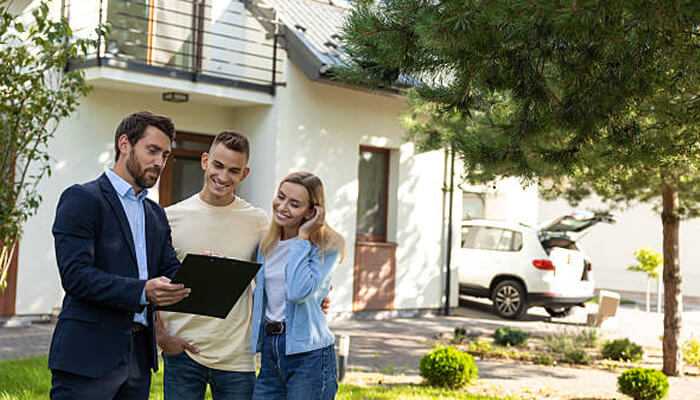 Market conditions in scottsdale 1 | tycoonstory media Real estate agent showing property details to a couple outside a modern home, representing client consultations in scottsdale real estate.