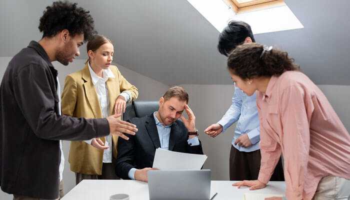 The courage to disappoint - tycoonstory | tycoonstory media Overwhelmed businessman surrounded by colleagues, showing the need for sustainable leadership to balance success and avoid burnout.