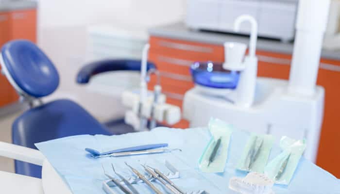 Dental implants and snoring guards A clean and modern dental clinic setup with dental tools arranged on a tray and a blue chair in the background, representing advanced treatments such as dental implants and snoring guards.