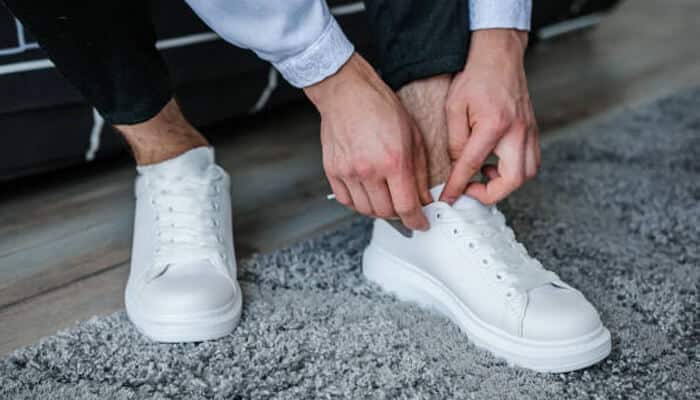 Timeless wardrobe staples Close-up of a person tying white sneakers, showcasing a modern and comfortable option as part of timeless wardrobe staples for everyday wear.