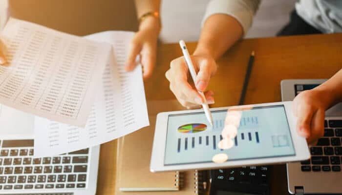 Signage roi Hands reviewing charts on a tablet and printed sheets, analyzing marketing performance and measuring signage roi.